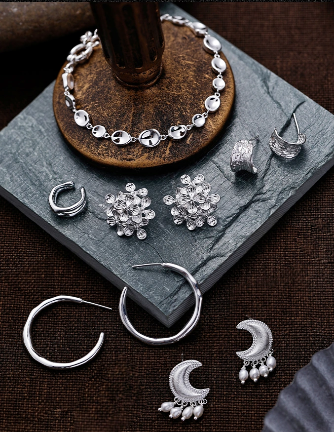 Silver-colored hoops, crescent earrings, and sculptural jewelry on stone